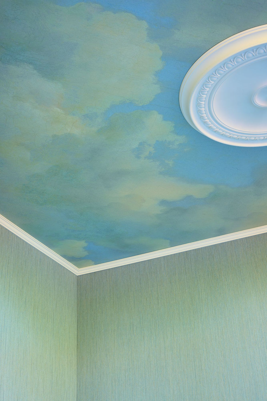 Cumulus Blue mural by Eijffinger, a painted sky of blue and white clouds covering a ceiling around a plaster ceiling rose