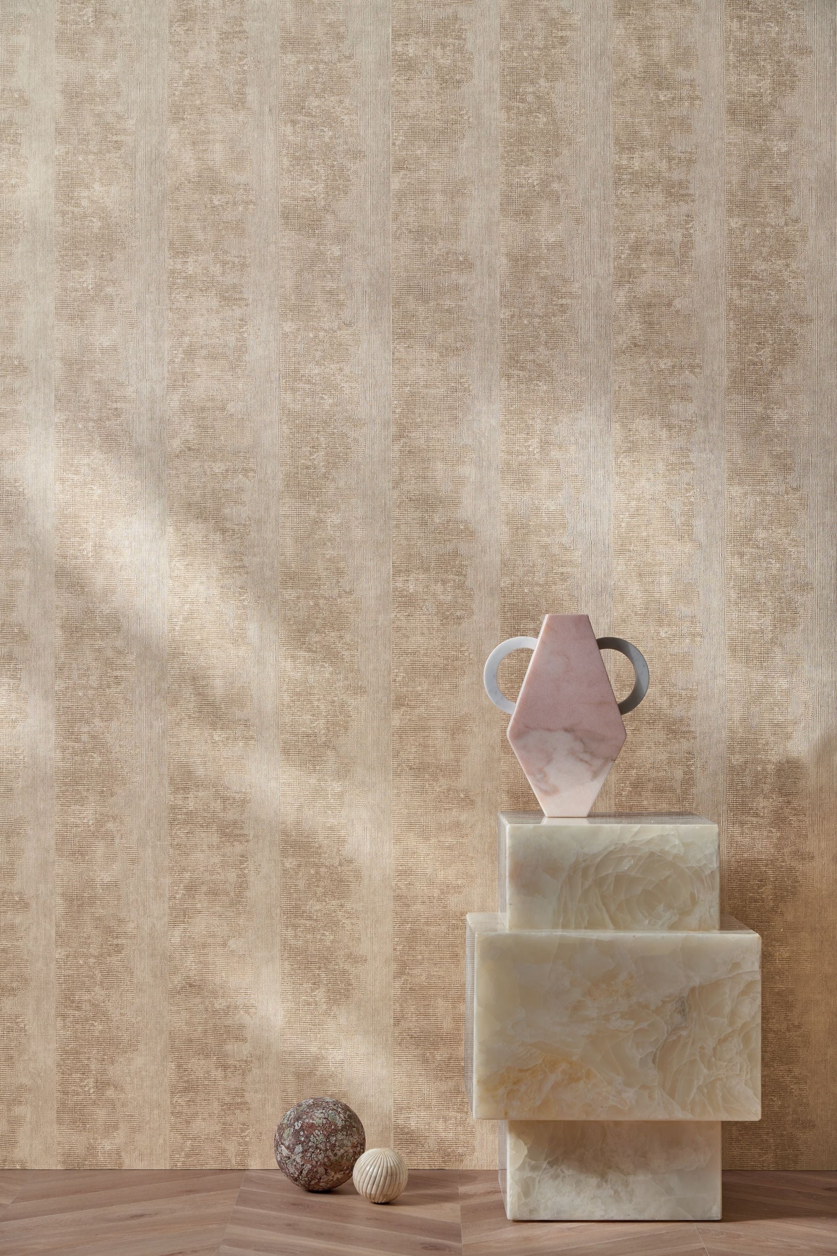 Zumaia Sable wallpaper by Casamance, warm sandstone strata in raked light behind a plinth of pale stone blocks and pebbles