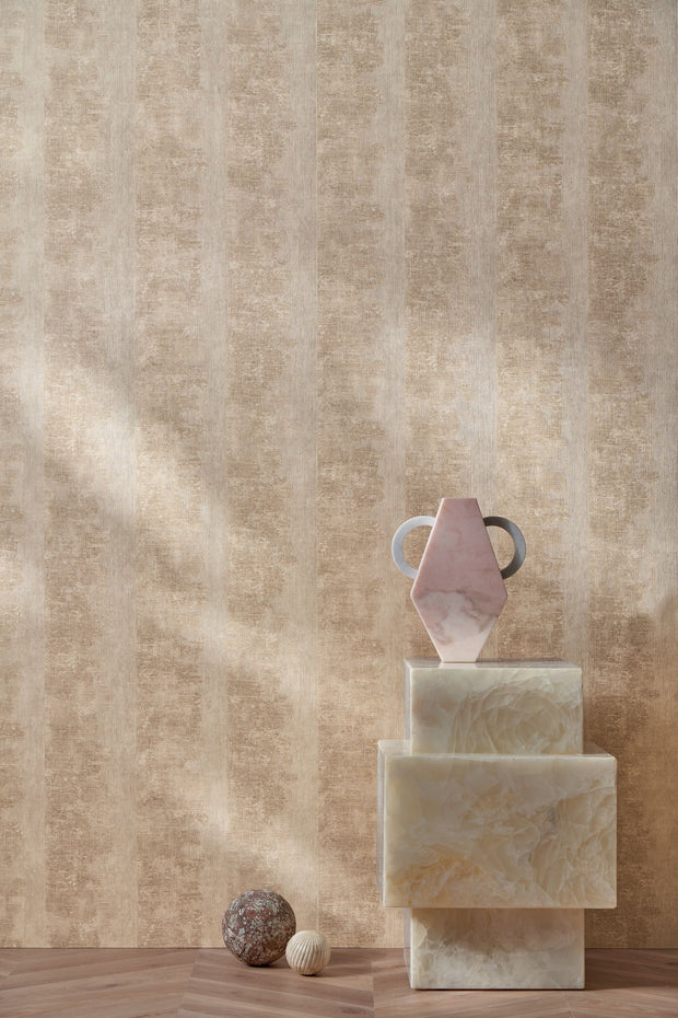 Zumaia Sable wallpaper by Casamance, warm sandstone strata in raked light behind a plinth of pale stone blocks and pebbles