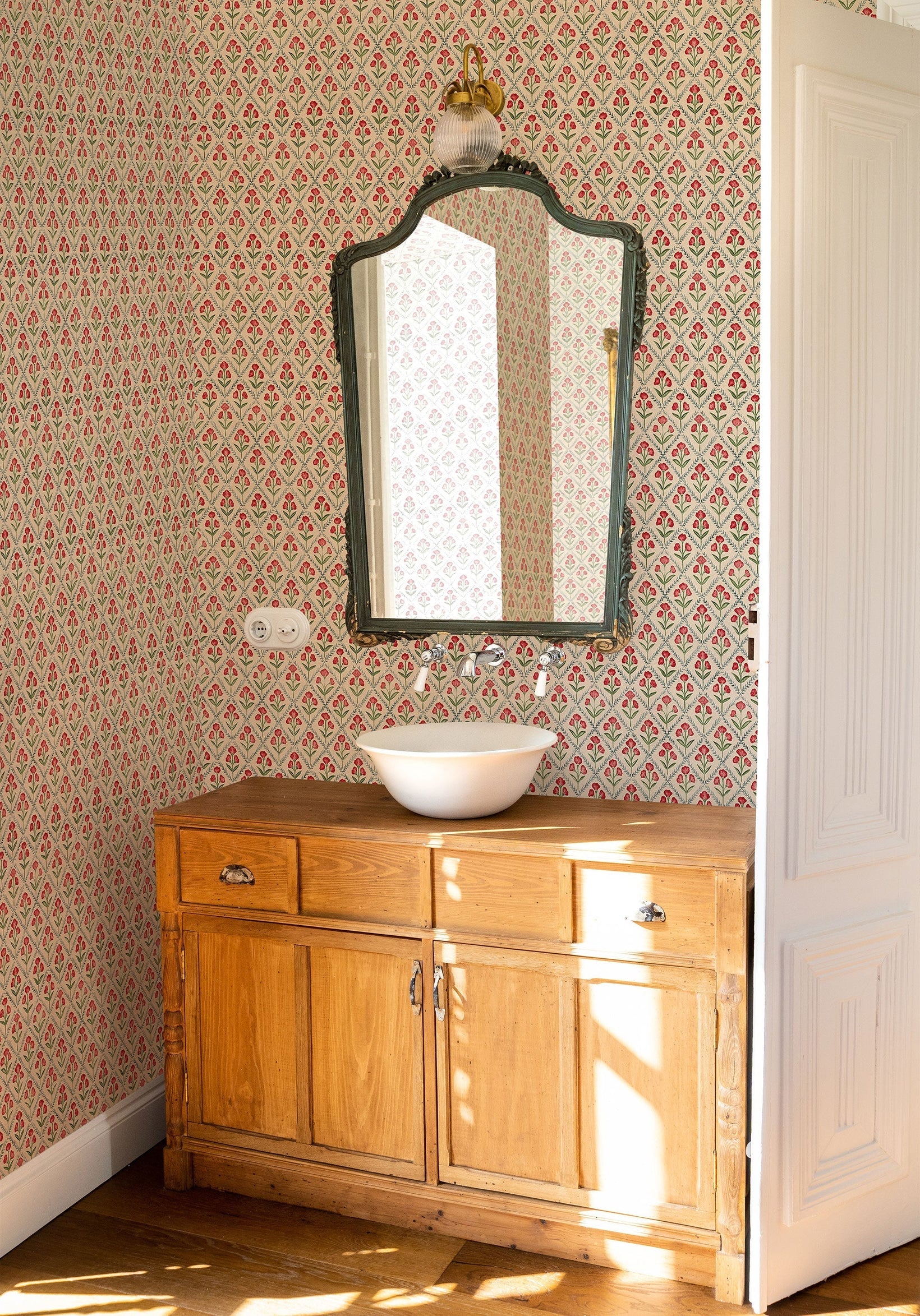 Poppy Red wallpaper by Coordonne, a fine Victorian poppy print in warm red above a wooden vanity and a shaped mirror