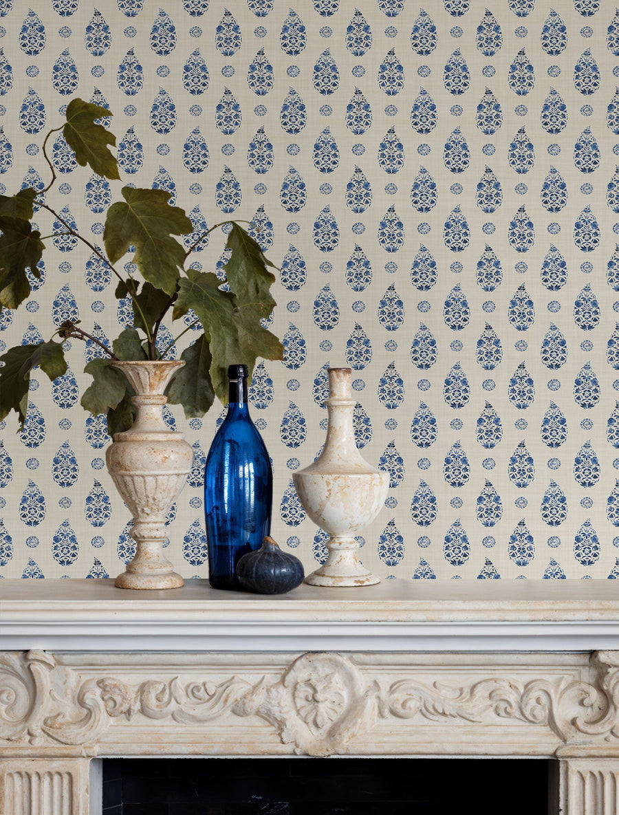 Paisley Blue wallpaper by Coordonne, a blue boteh repeat above a carved stone mantelpiece with blue glass and stone urns