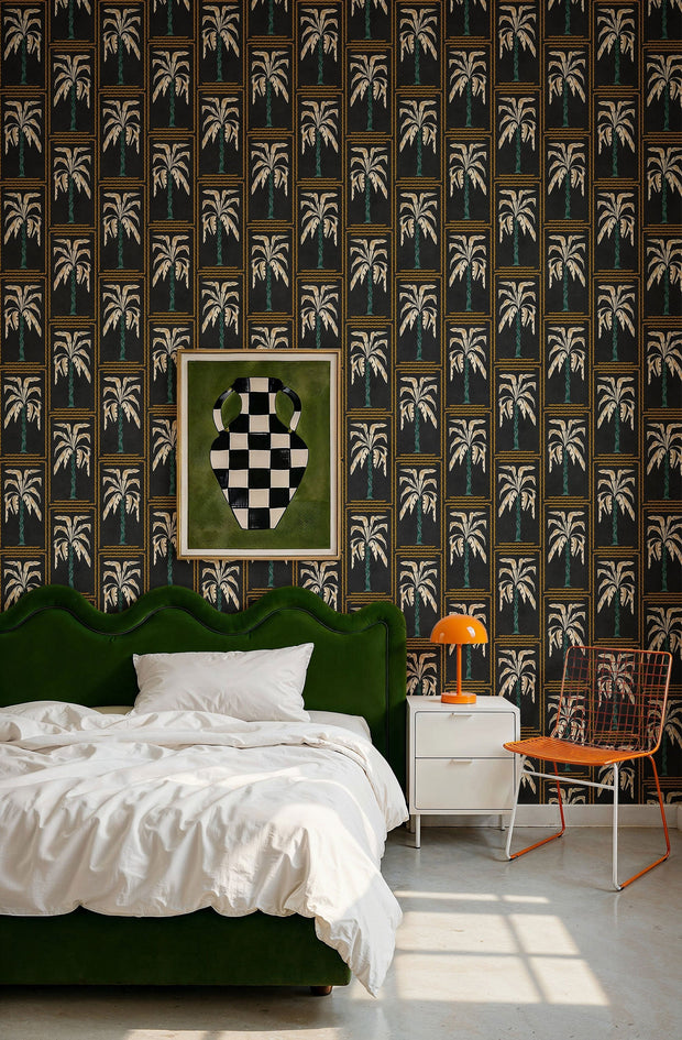 Veraneo Noir wallpaper by Coordonne, gold palm columns on black behind a green velvet bed and an orange lamp