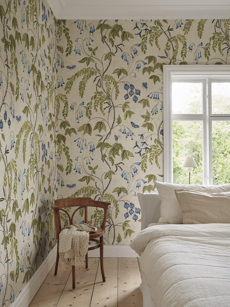 Ottilia Olive Green mural by Sandberg, a climbing olive-green leaf trail in a pale bedroom corner with a window and a bentwood chair